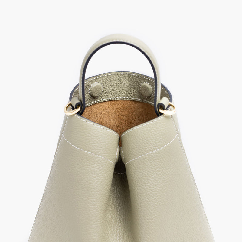 Close up of STOW London's Mini Curve in Pale Green pebbled leather featuring hidden magnets, suede lining and gold hardware on a light grey background 