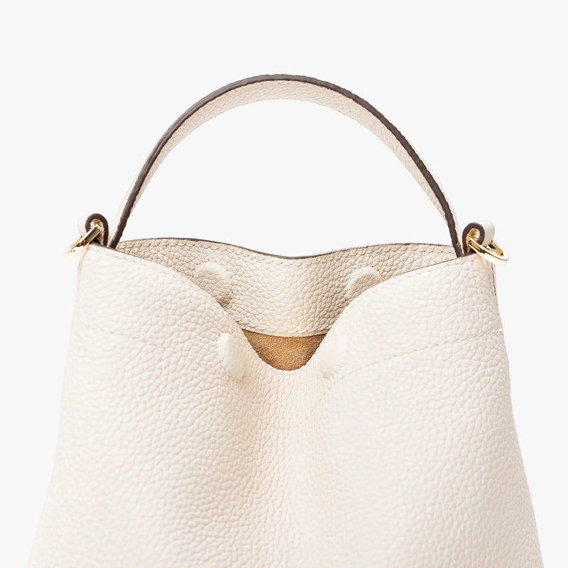 Close up of STOW London's Mini Curve in Spring Moon pebbled leather featuring the hidden magnetic closures, gold hardware and suede interior lining on a light grey background 