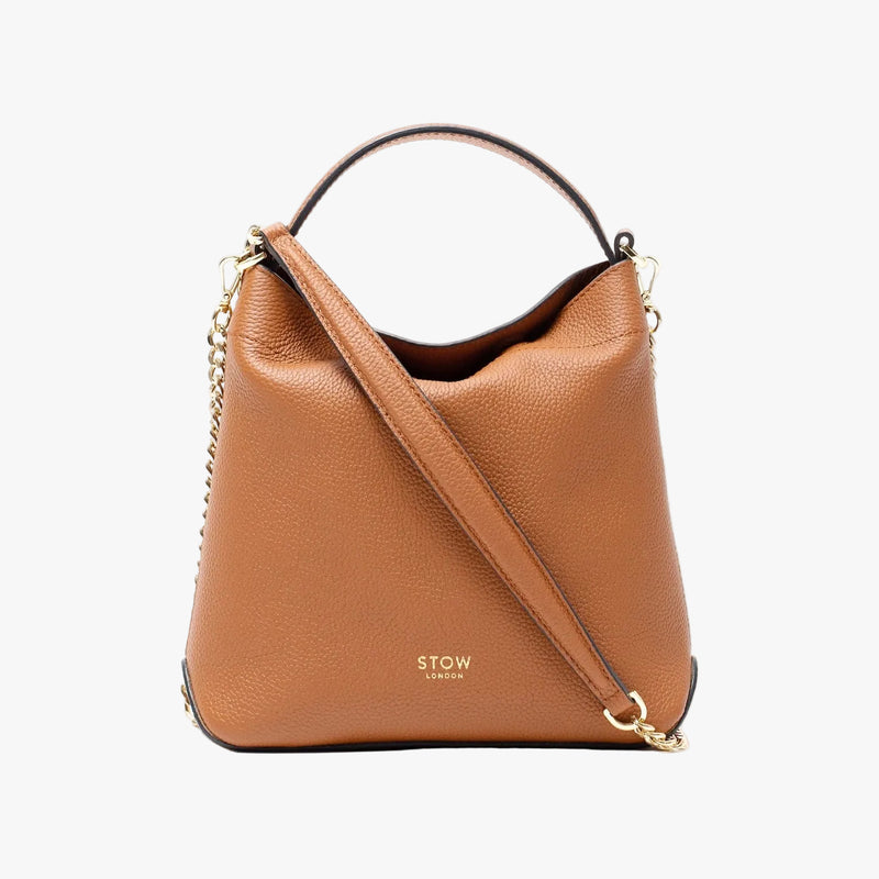 STOW London's Mini Curve in Earth tan pebbled leather and detachable gold chain crossbody strap on a light grey background shaped as a flap bag
