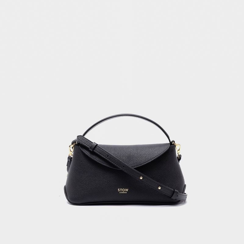 STOW London's Mini East West in Black pebbled leather and detachable crossbody strap featuring gold-coated stainless steel hardware on a light grey background