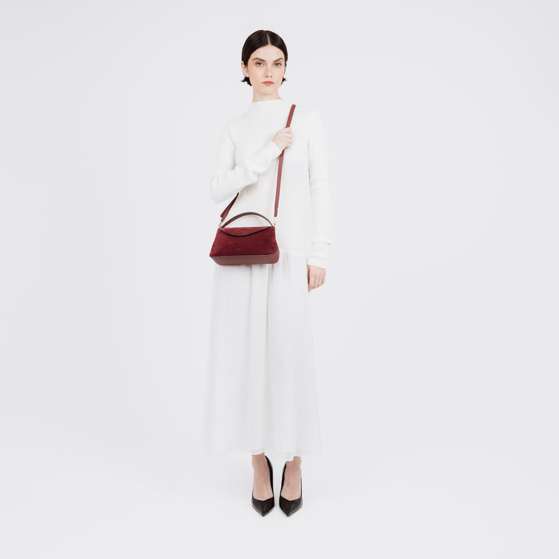 Model wearing STOW London's Mini East West bag in Burgundy Suede leather  crossbody featuring gold-coated stainless steel hardware on a white background
