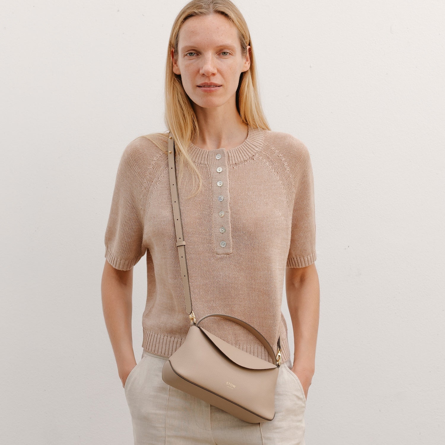 Model wearing STOW London's Mini East West in Camel pebbled leather crossbody featuring gold-coated stainless steel hardware