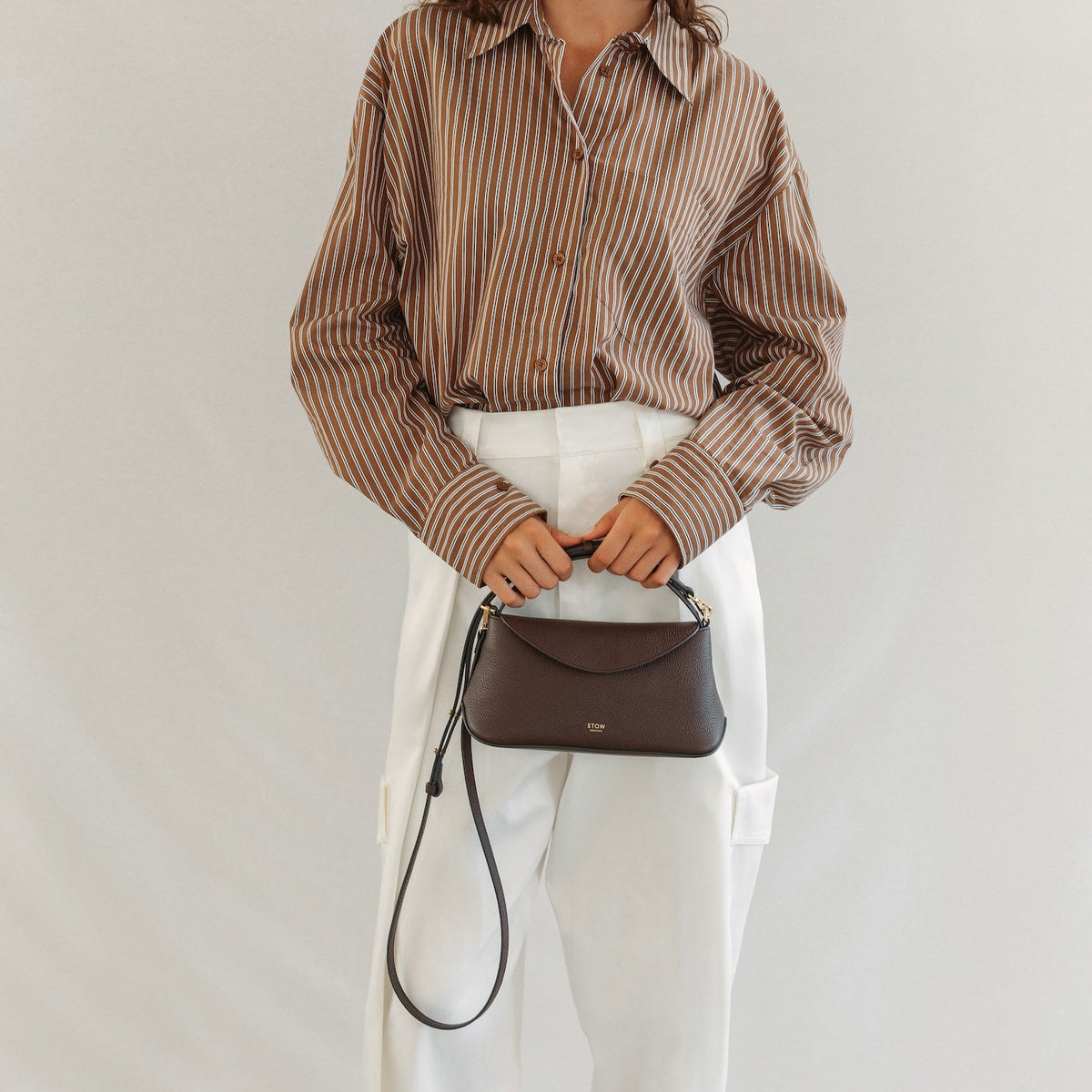 Model holding STOW London's Mini East West in Espresso pebbled leather featuring gold-coated stainless steel hardware 