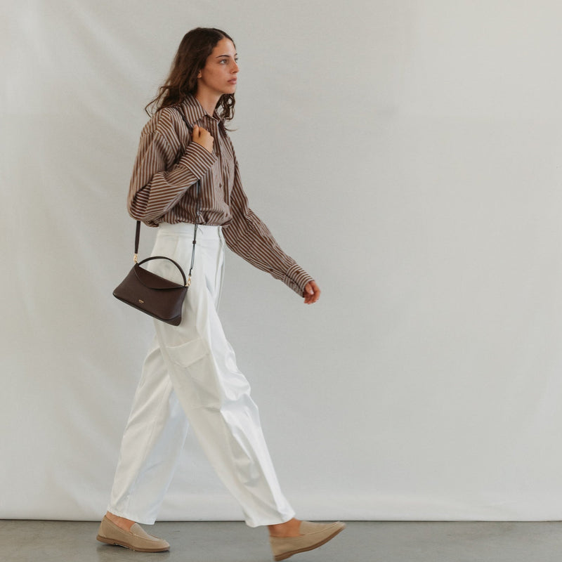Model wearing STOW London's Mini East West in Espresso pebbled leather featuring gold-coated stainless steel hardware 