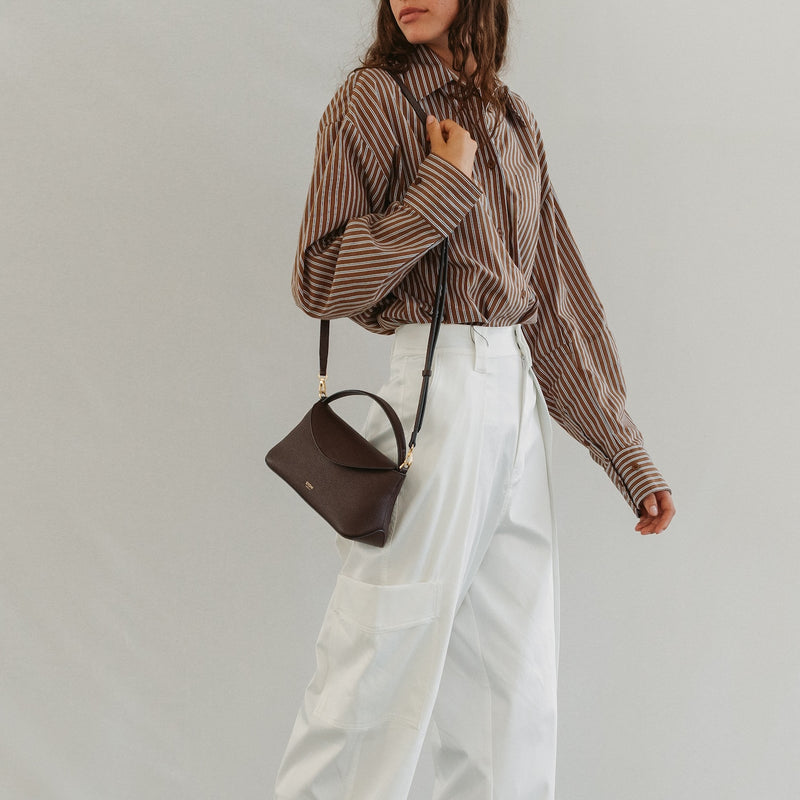 Model wearing STOW London's Mini East West in Espresso pebbled leather featuring gold-coated stainless steel hardware 