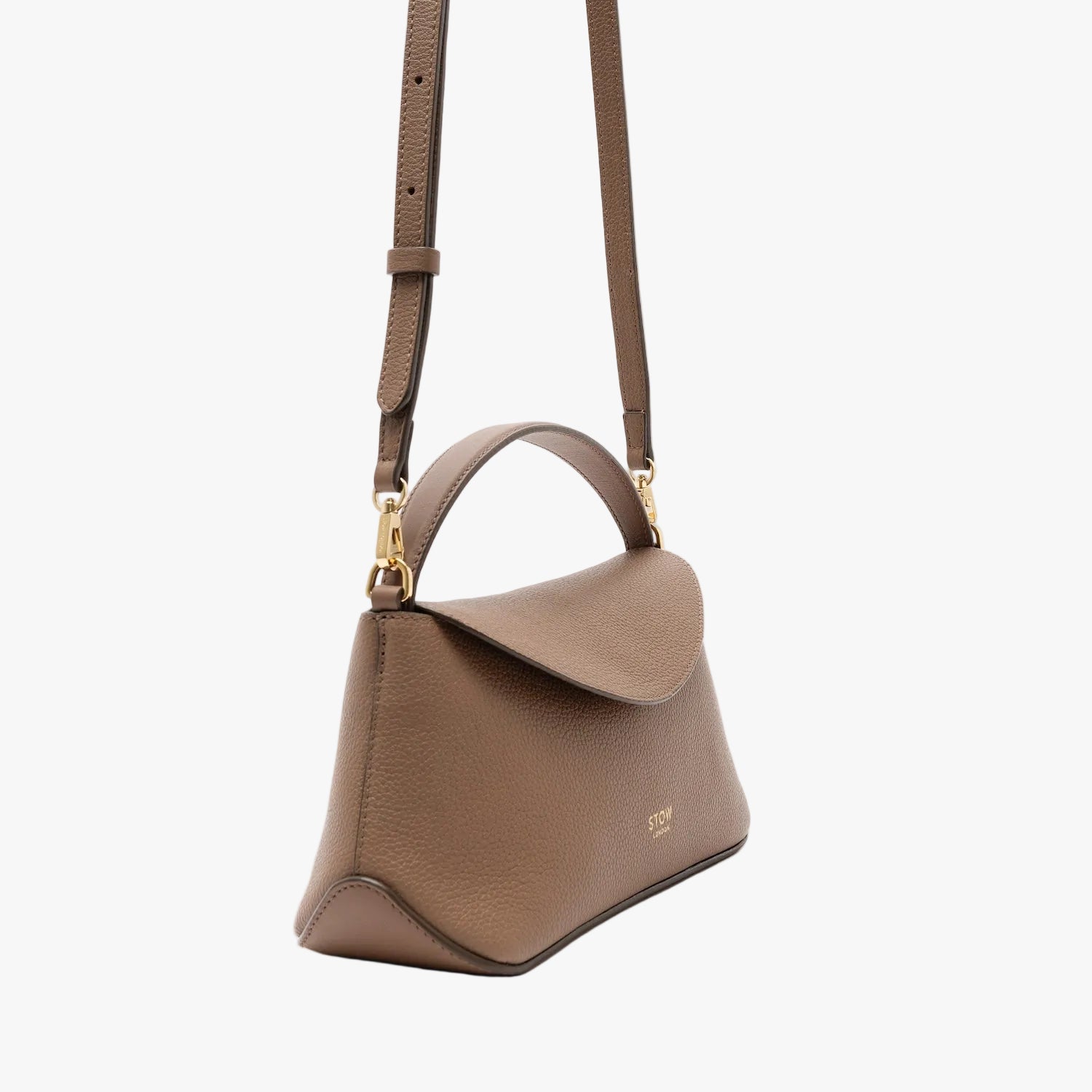 Off-axis view of STOW London's Mini East West in Mocha pebbled leather and crossbody strap featuring gold-coated stainless steel hardware on a light grey background 