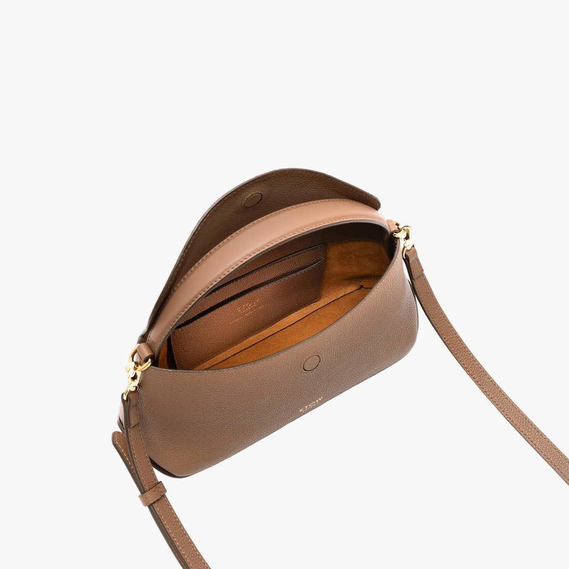 Overhead shot STOW London's Mini East West in Mocha pebbled leather with flap open showing suede interior and leather slip pocket featuring gold-coated stainless steel hardware and crossbody strap on a light grey background 