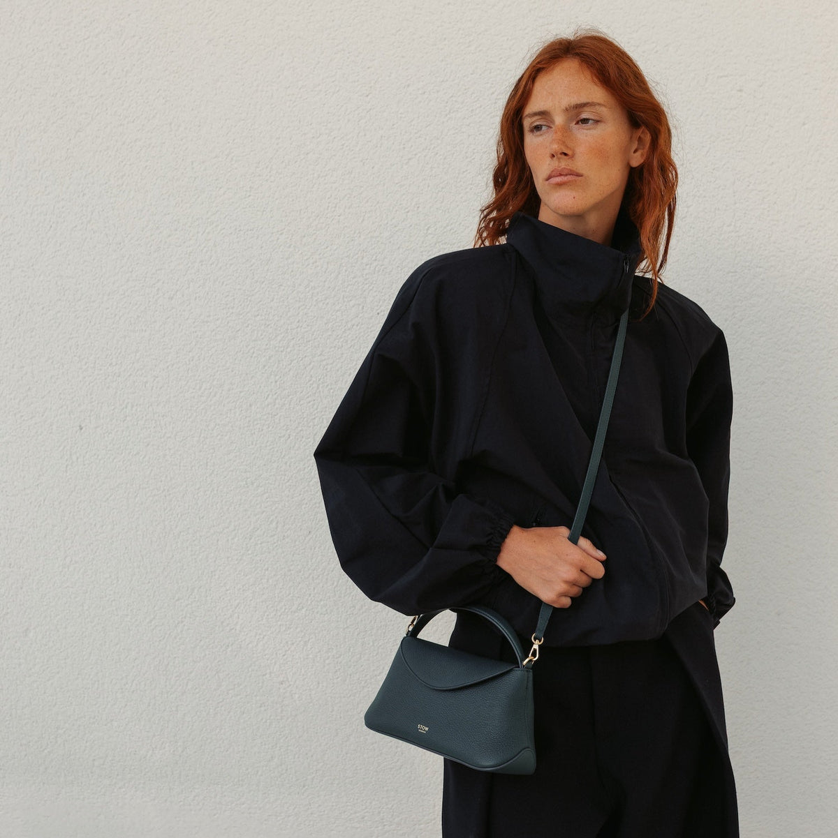 Model in a full black outfit wearing STOW London's Mini East West in New Forest pebbled leather crossbody featuring gold-coated stainless steel hardware 