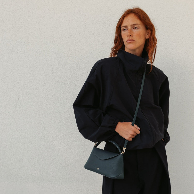 Model in a full black outfit wearing STOW London's Mini East West in New Forest pebbled leather crossbody featuring gold-coated stainless steel hardware 