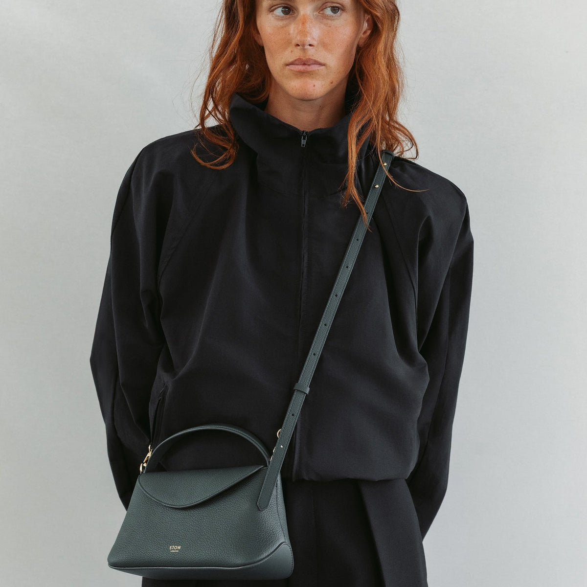 Model in a full black outfit wearing STOW London's Mini East West in New Forest pebbled leather crossbody featuring gold-coated stainless steel hardware 