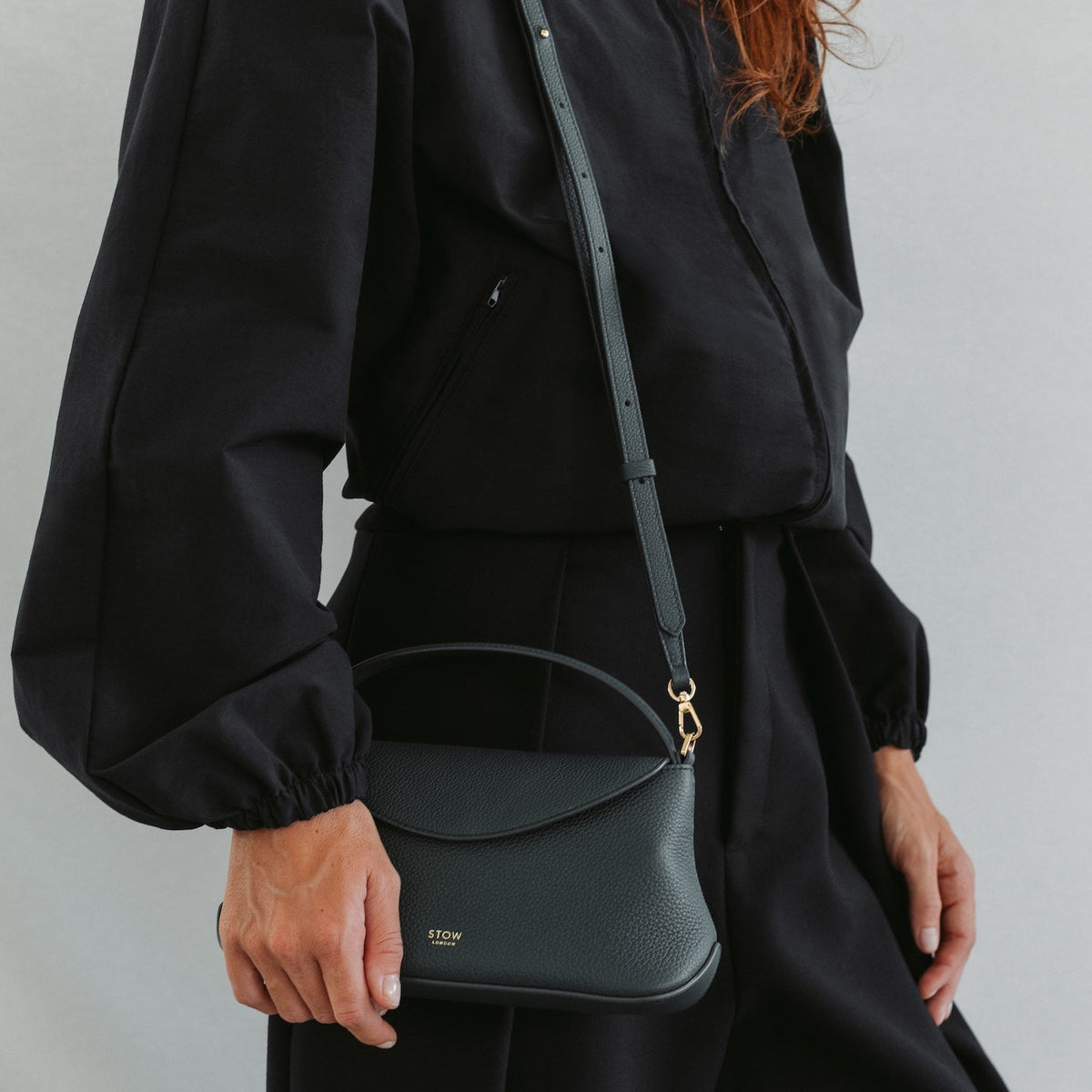 Model in a full black outfit wearing STOW London's Mini East West in New Forest pebbled leather featuring gold-coated stainless steel hardware 