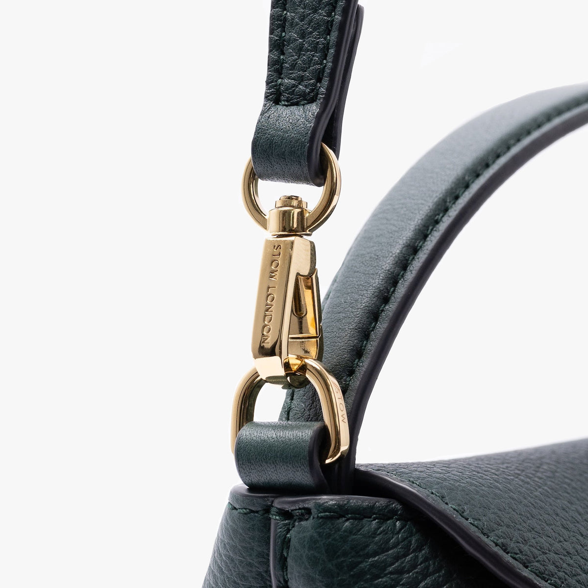 Close up of the gold-coated stainless steel hardware on STOW London's Mini East West in New Forest pebbled leather on a light grey background 