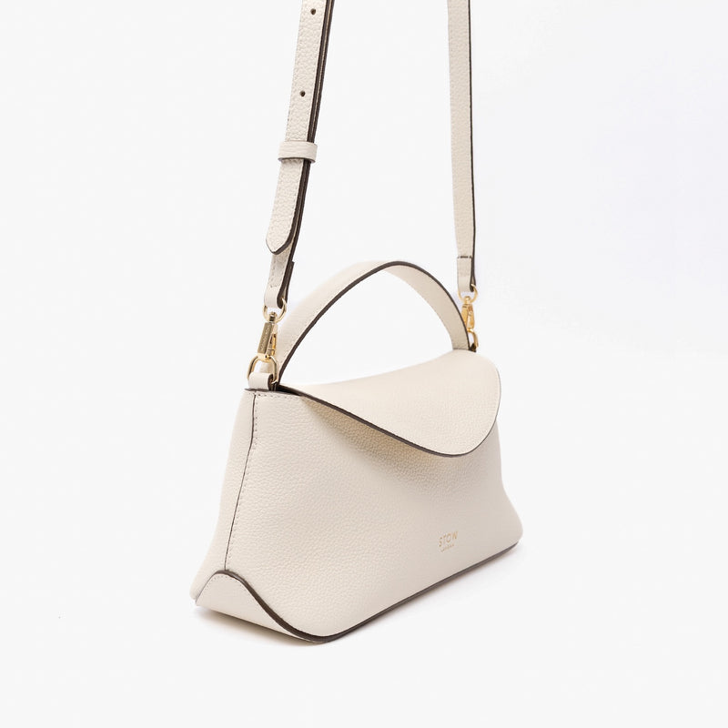 Off-axis view of STOW London's Mini East West in Spring Moon pebbled leather and detachable crossbody strap featuring gold-coated stainless steel hardware on a light grey background