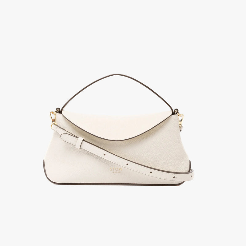 STOW London's Mini East West in Spring Moon pebbled leather featuring its crossbody strap and gold-coated stainless steel hardware on a light grey background