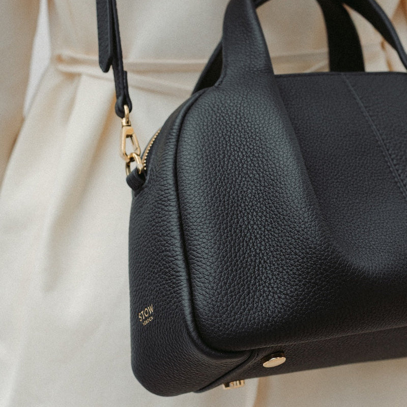 Close up of model wearing STOW London's Mini Bowling in Black pebbled leather featuring a pleated front panel and gold-coated stainless steel hardware