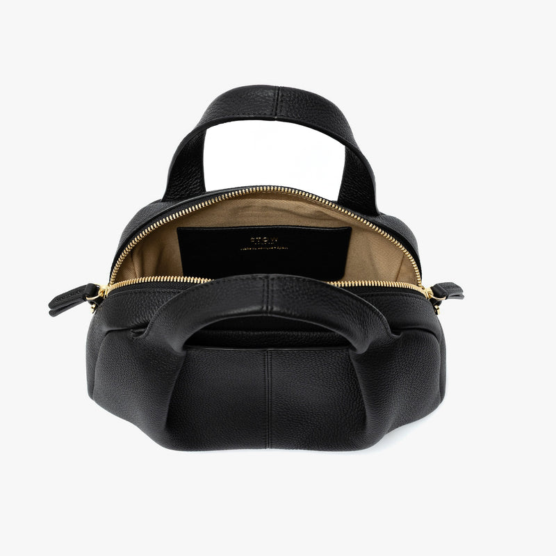 STOW London's Mini Bowling bag in Black pebbled leather with zips open showing the light beige interior lining and slip pocket featuring gold-coated stainless steel hardware on a light grey background