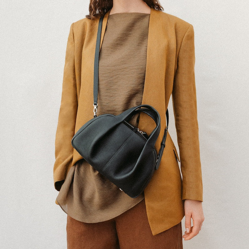 Model wearing STOW London's Mini Bowling in Black pebbled leather crossbody featuring a pleated front panel and silver stainless steel hardware