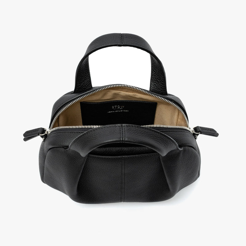 STOW London's Mini Bowling bag in Black pebbled leather with zips open showing the light beige cotton interior lining and slip pocket featuring silver stainless steel hardware on a light grey background