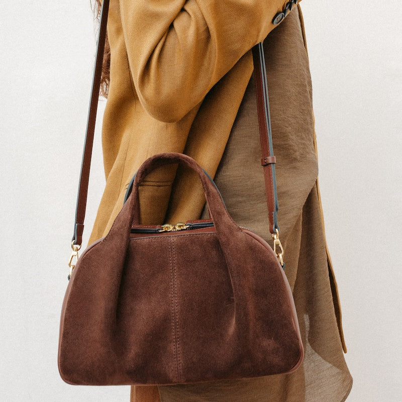 Model wearing STOW London's Mini Bowling in Chocolate suede leather on her shoulder featuring a pleated front panel and gold-coated stainless steel hardware