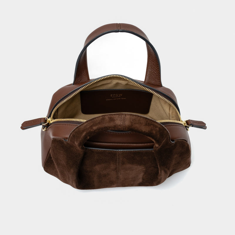 STOW London's Mini Bowling bag in Chocolate suede and smooth leather with zips open showing light beige interior lining and slip pocket featuring gold-coated stainless steel hardware on a light grey background