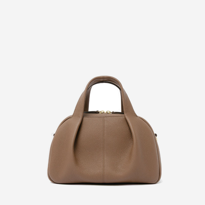 STOW London's Mini Bowling bag in Mocha pebbled leather featuring a pleated front panel and gold-coated stainless steel hardware on a light grey background
