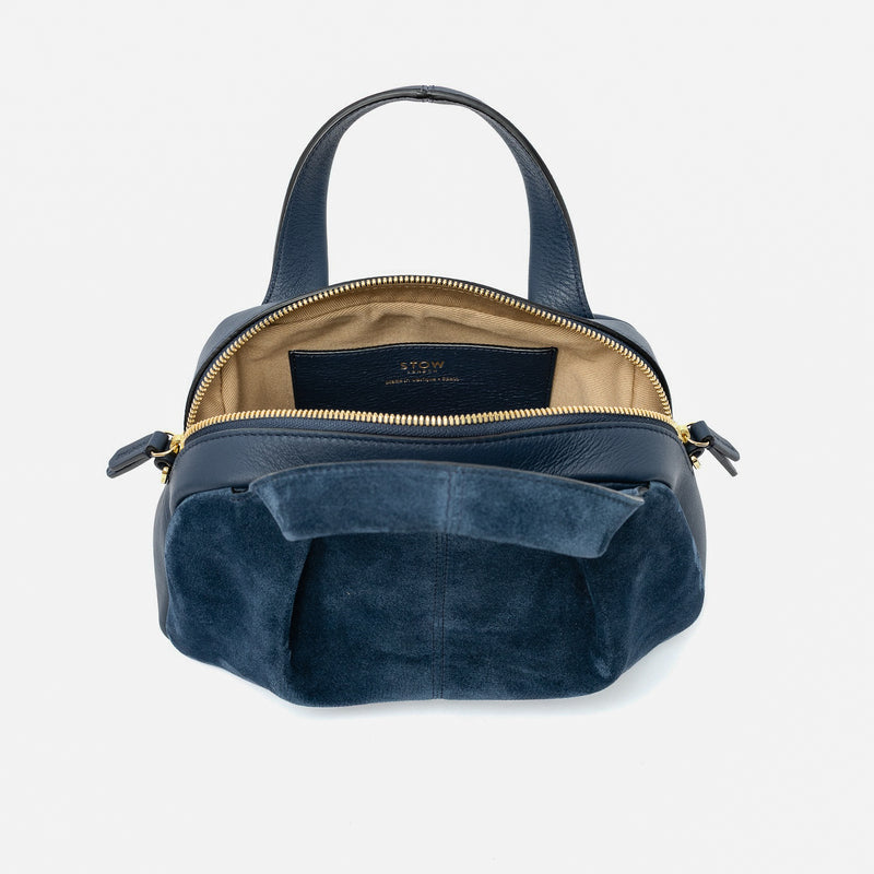 STOW London's Mini Bowling bag in Navy suede and smooth leather with zipper open showing the cotton interior lining and the internal slip pocket featuring gold-coated stainless steel hardware on a light grey background