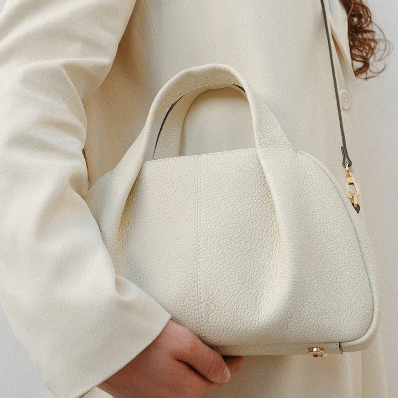 Close up of model wearing STOW London's Mini Bowling bag in Spring Moon pebbled leather crossbody featuring a pleated front panel, detachable crossbody strap and gold-coated stainless steel hardware and feet on base