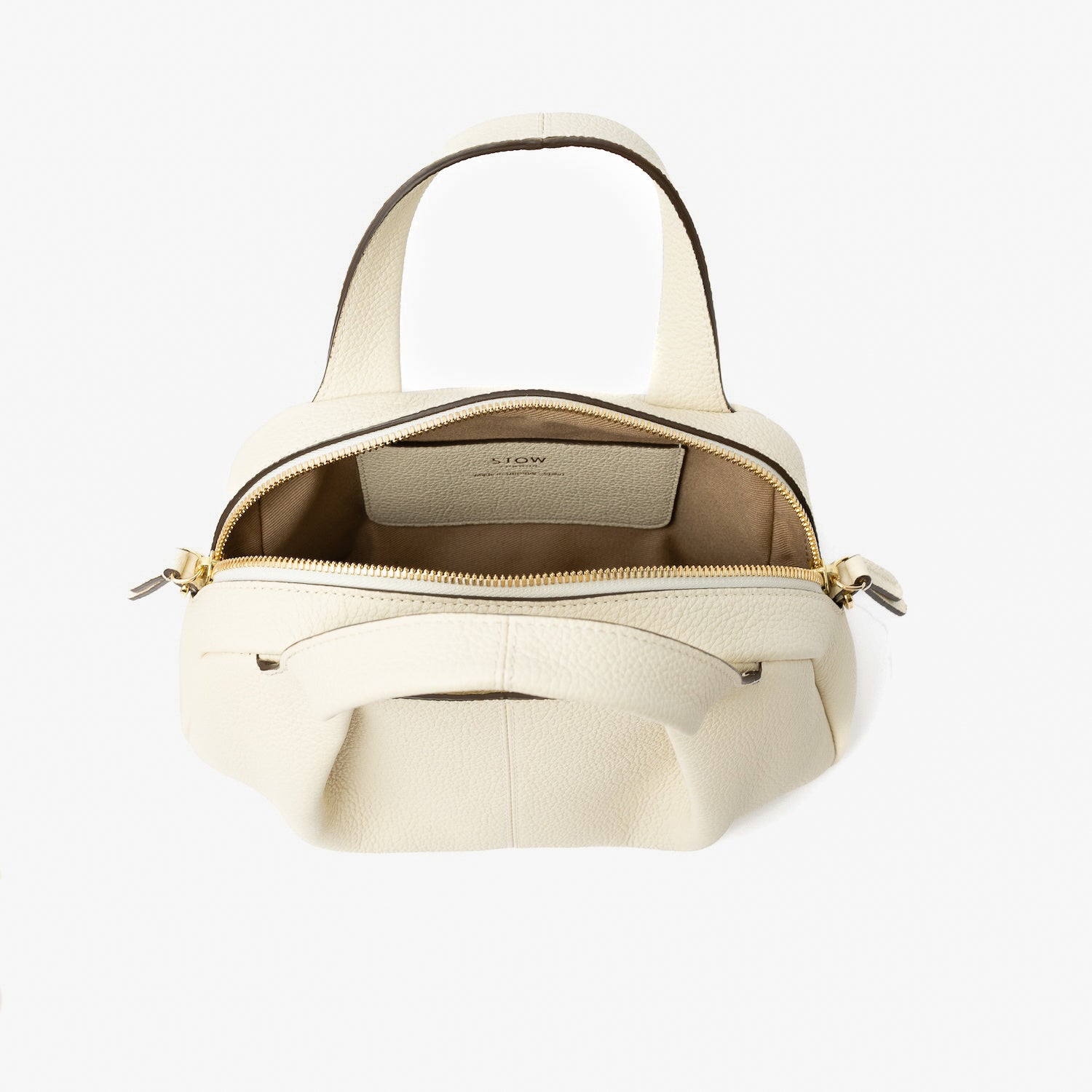 STOW London's Mini Bowling bag in Spring Moon pebbled leather with zip open showing light beige cotton interior lining and slip pocket, featuring gold-coated stainless steel hardware on a light grey background