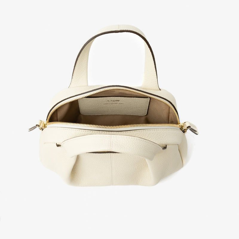 STOW London's Mini Bowling bag in Spring Moon pebbled leather with zip open showing light beige cotton interior lining and slip pocket, featuring gold-coated stainless steel hardware on a light grey background