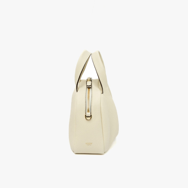 Side view of STOW London's Mini Bowling bag in Spring Moon pebbled leather featuring the zip closure and small gold logo on a light grey background
