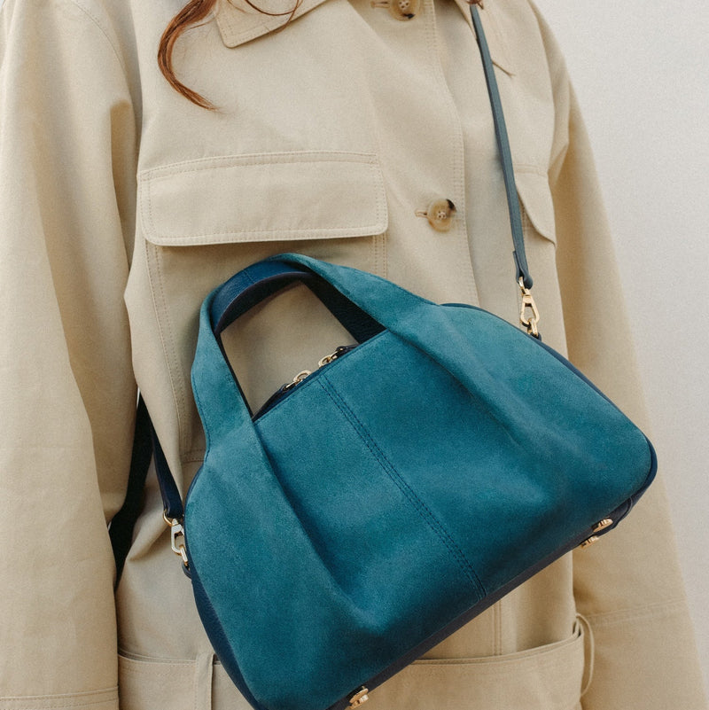 Model wearing STOW London's Mini Bowling bag in Ocean Teal suede and smooth leather featuring a pleated front panel, detachable crossbody strap and gold-coated stainless steel hardware 