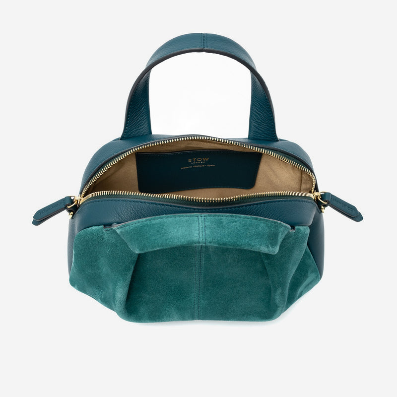 STOW London's Mini Bowling bag in Ocean Teal suede and smooth leather with zipper open showing the light beige cotton interior lining and slip pocket, featuring gold-coated stainless steel hardware on a light grey background