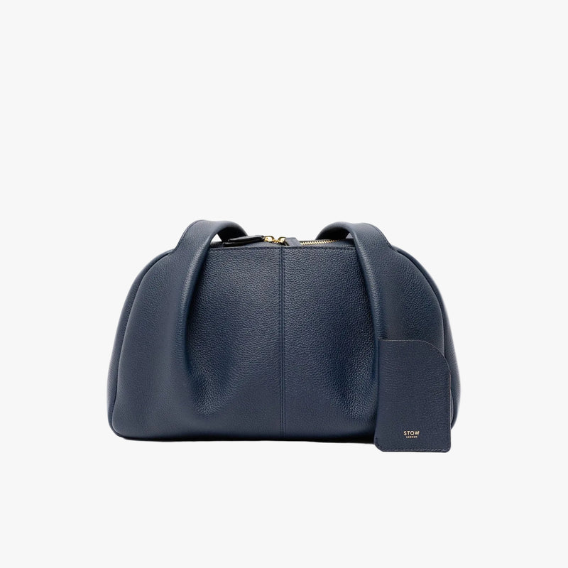 STOW London's Mini Cardholder in Navy pebbled leather with the matching Bowling Bag on a light grey background featuring a small gold embossed logo on the front bottom