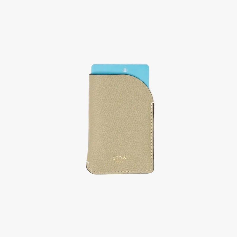 STOW London's Mini Cardholder in Pale Green pebbled leather with a blue card inside on a light grey background featuring a small gold embossed logo on the front bottom