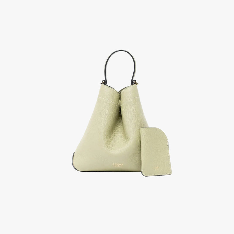 STOW London's Mini Cardholder in Pale Green pebbled leather alongside the matching Mini Curve bag on a light grey background featuring a small gold embossed logo on both front panels