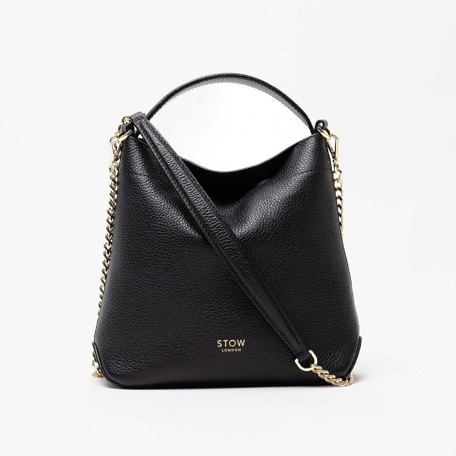 STOW London's Mini Curve in Black pebbled leather and detachable gold chain crossbody strap styled asa flap bag on a light grey background 