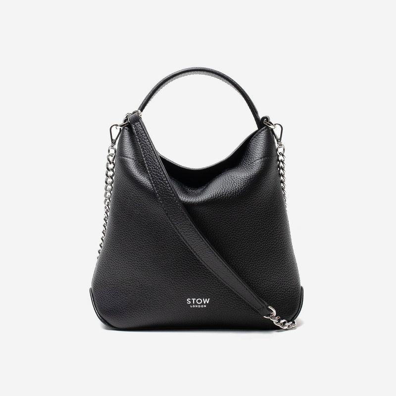 Stow London's Mini Curve in Black pebbled leather and detachable silver chain crossbody strap styled as a flap bag on a light grey background 