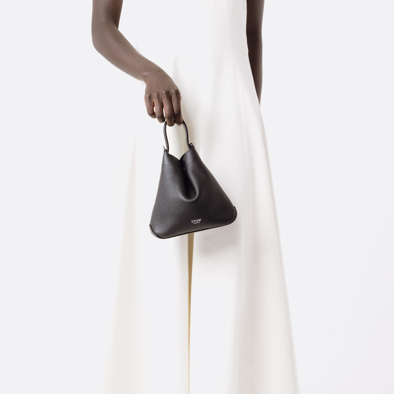 Model holding Stow London's Mini Curve in Black pebbled leather by top handle on a white background 