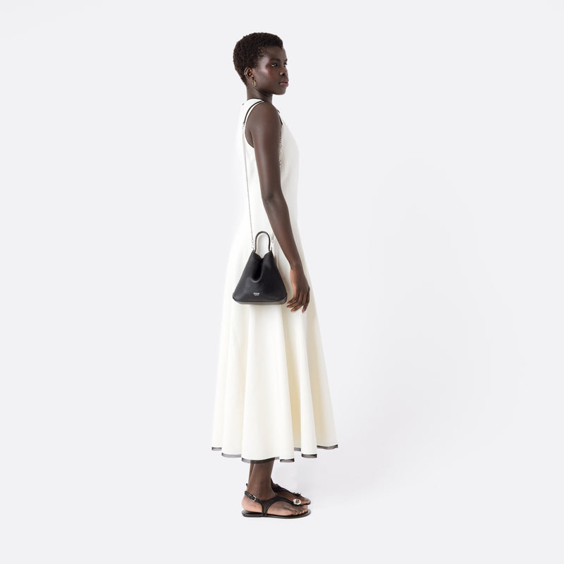 Model wearing Stow London's Mini Curve in Black pebbled leather on her shoulder by the detachable silver chain crossbody strap on a white background 