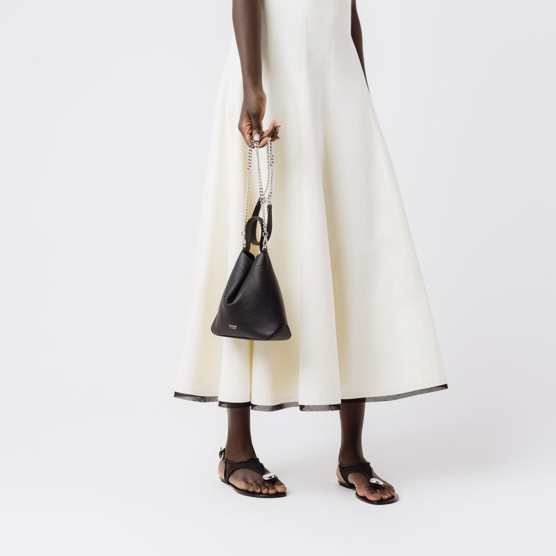 Model holding Stow London's Mini Curve in Black pebbled leather by the detachable silver chain crossbody strap on a white background 