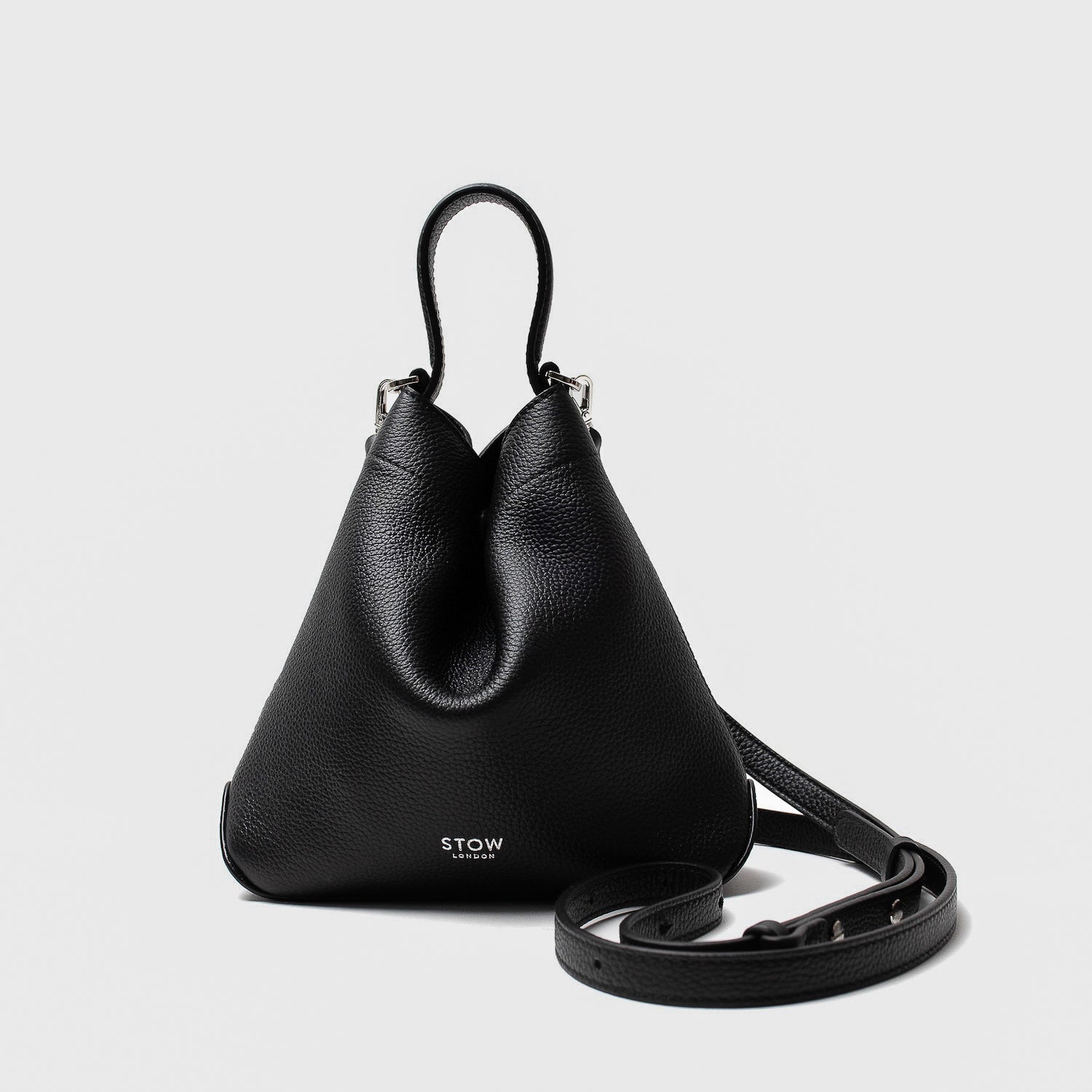 STOW London's Mini Curve in Black pebbled leather and detachable leather crossbody strap on a light grey background 