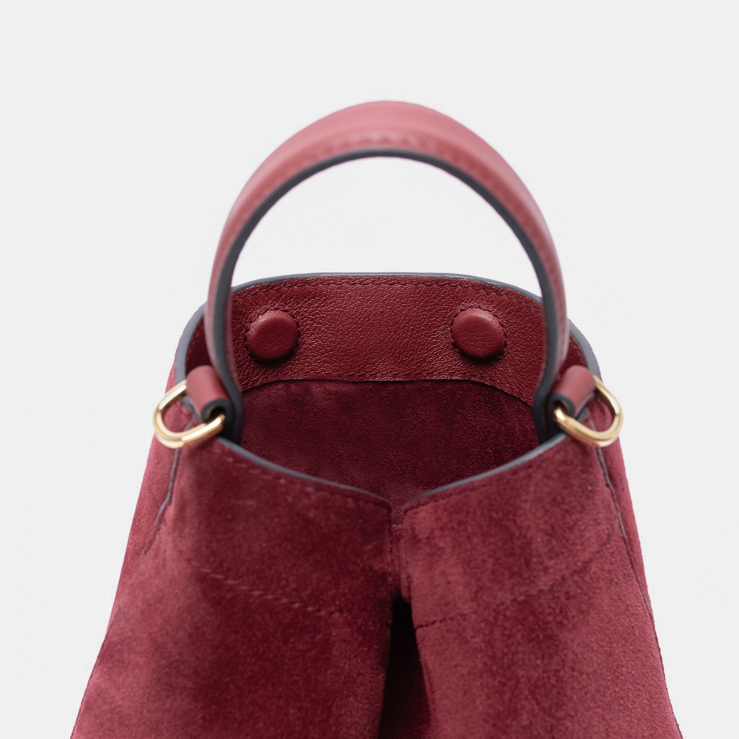Close up of Stow London's Mini Curve in Burgundy suede leather featuring hidden magnets, suede lining and gold hardware on a light grey background 