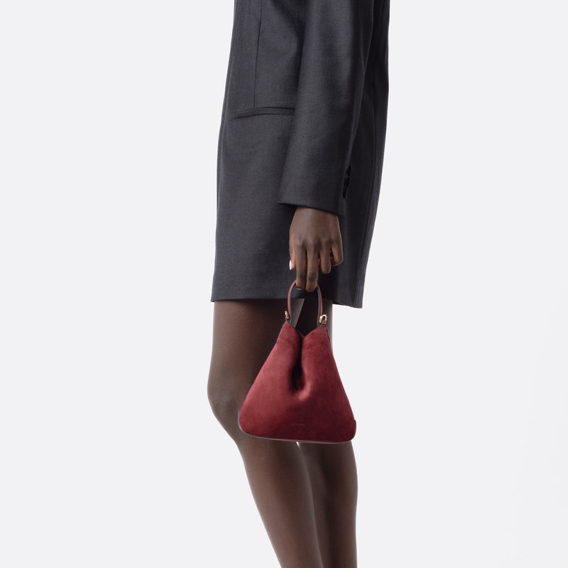 Model holding Stow London's Mini Curve in Burgundy suede leather at her side on a white background 