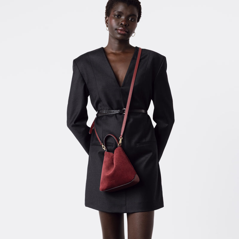 Model wearing STOW London's Mini Curve in Burgundy suede leather with the detachable leather crossbody strap on a white background 