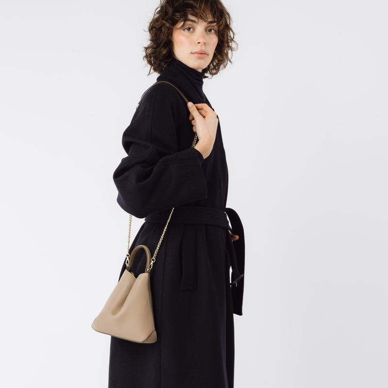 Model wearing STOW London's Mini Curve in Camel leather on her shoulder with the gold-plated chain on a white background