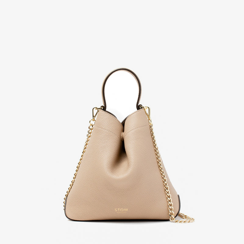 Stow London's Mini Curve in Camel pebbled leather and detachable gold chain crossbody strap on a light grey background 