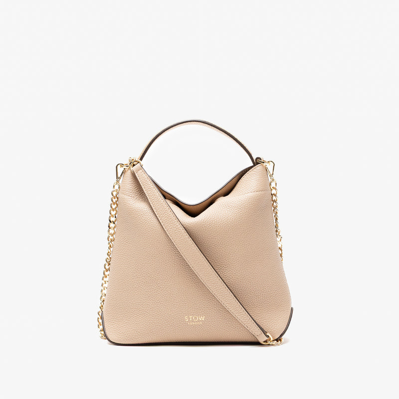 Stow London's Mini Curve in Camel pebbled leather and detachable gold chain crossbody strap styled as a flap bag on a light grey background 