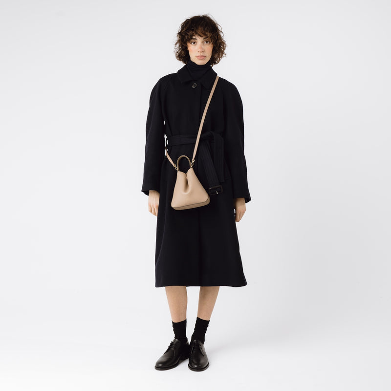 Model wearing STOW London's Mini Curve in Camel pebbled leather with the detachable leather crossbody strap on a white background 