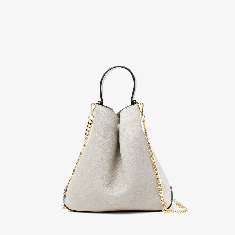 Stow London's Mini Curve in Cloud Grey pebbled leather and detachable gold chain crossbody strap on a light grey background 