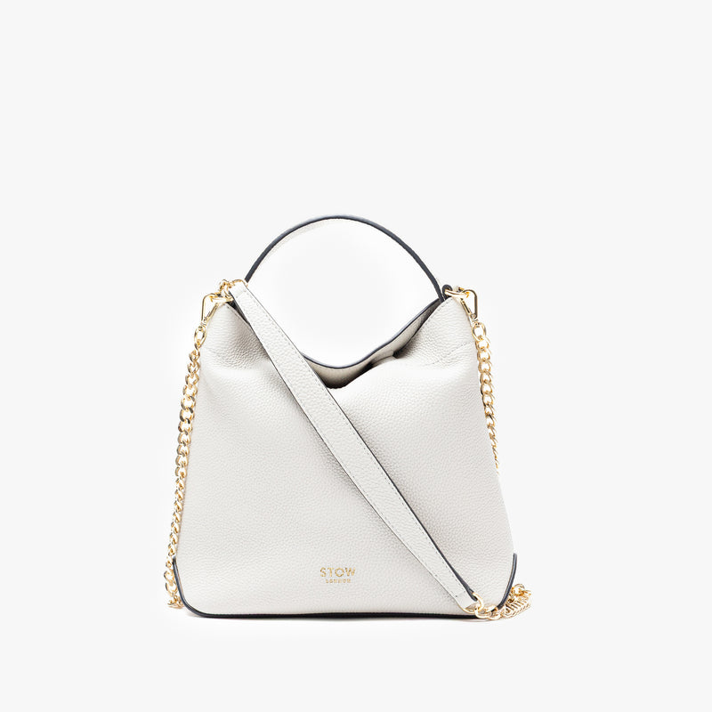 Stow London's Mini Curve in Cloud Grey pebbled leather and detachable gold chain crossbody strap on a light grey background 